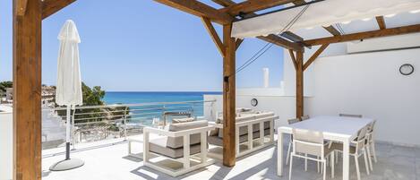 A terrace with white furniture, a white umbrella, and a view of the sea.