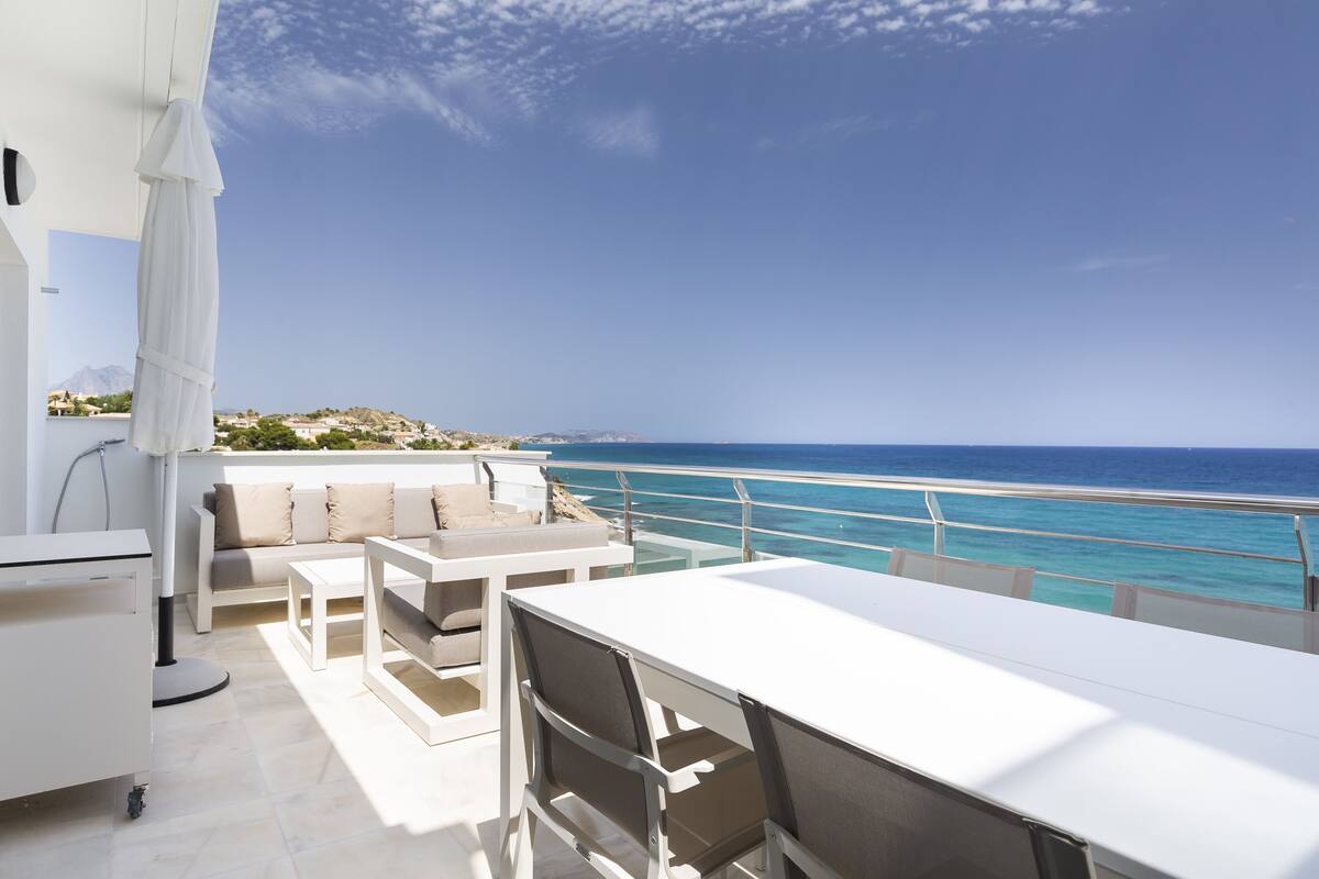 Een balkon met een witte tafel en stoelen, een bank en uitzicht op de oceaan.