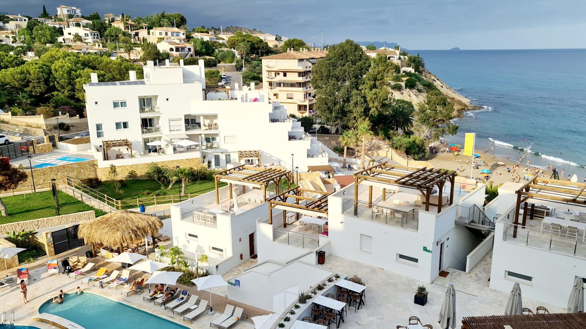 Zona de piscina al terrat amb gandules i ombrelles, una piscina i vista al mar i edificis de la ciutat.