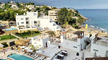 Zona de piscina al terrat amb gandules i ombrelles, una piscina i vista al mar i edificis de la ciutat.