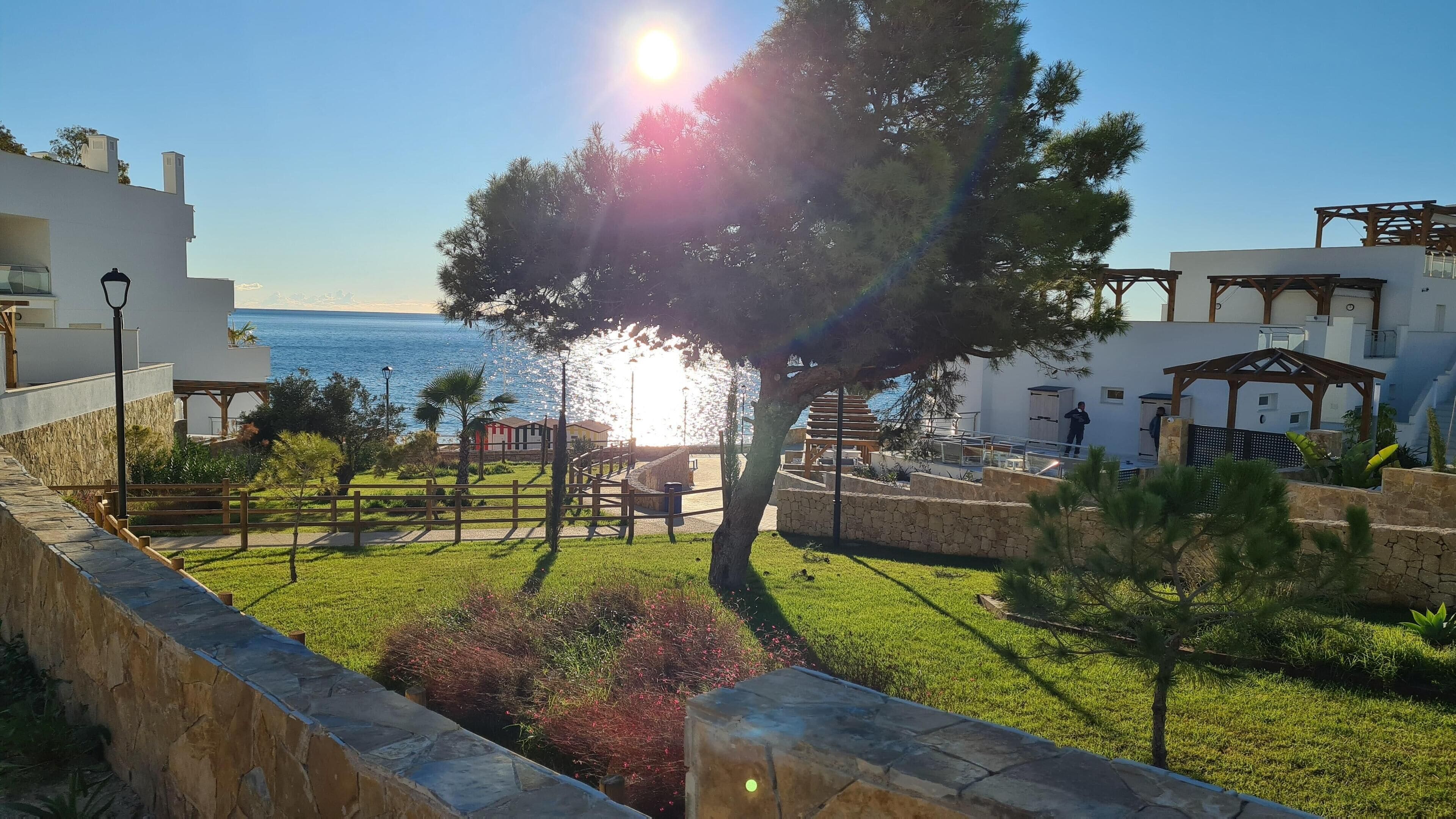 A coastal resort with a stone wall, grassy areas, and a wooden pergola.