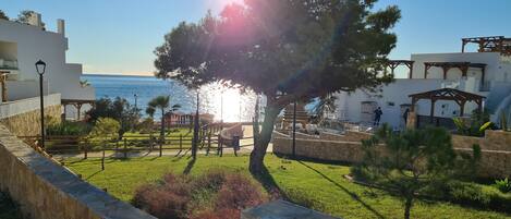 A coastal resort with a stone wall, grassy areas, and a wooden pergola.