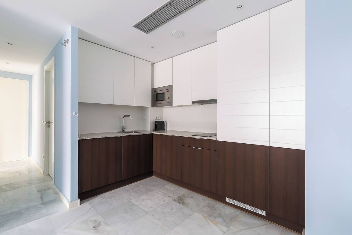 Een moderne keuken met donkere houten kastjes, witte aanrechtbladen en een ingebouwde magnetron.