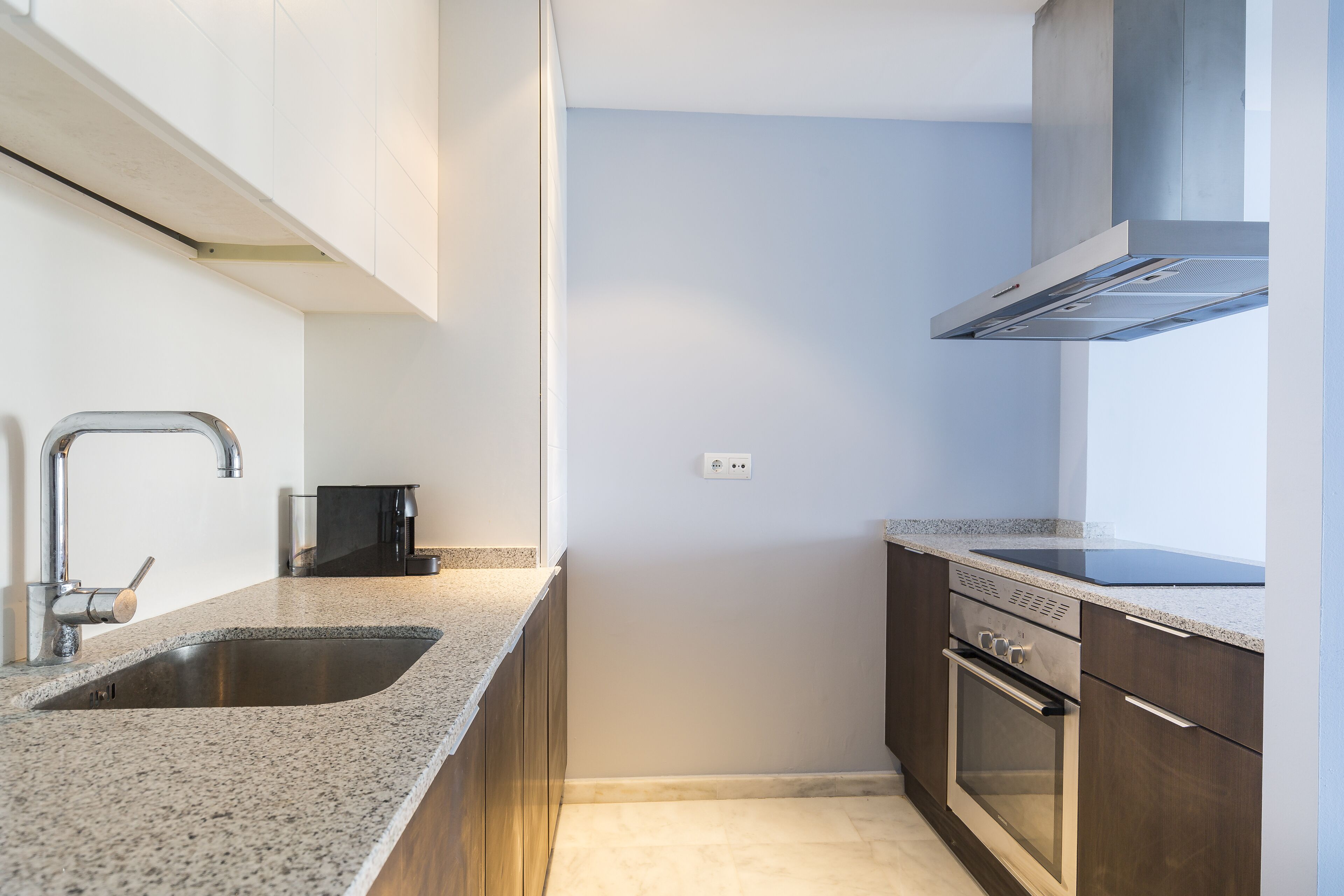 Una cocina moderna con encimera de granito, pileta de acero inoxidable y horno empotrado.