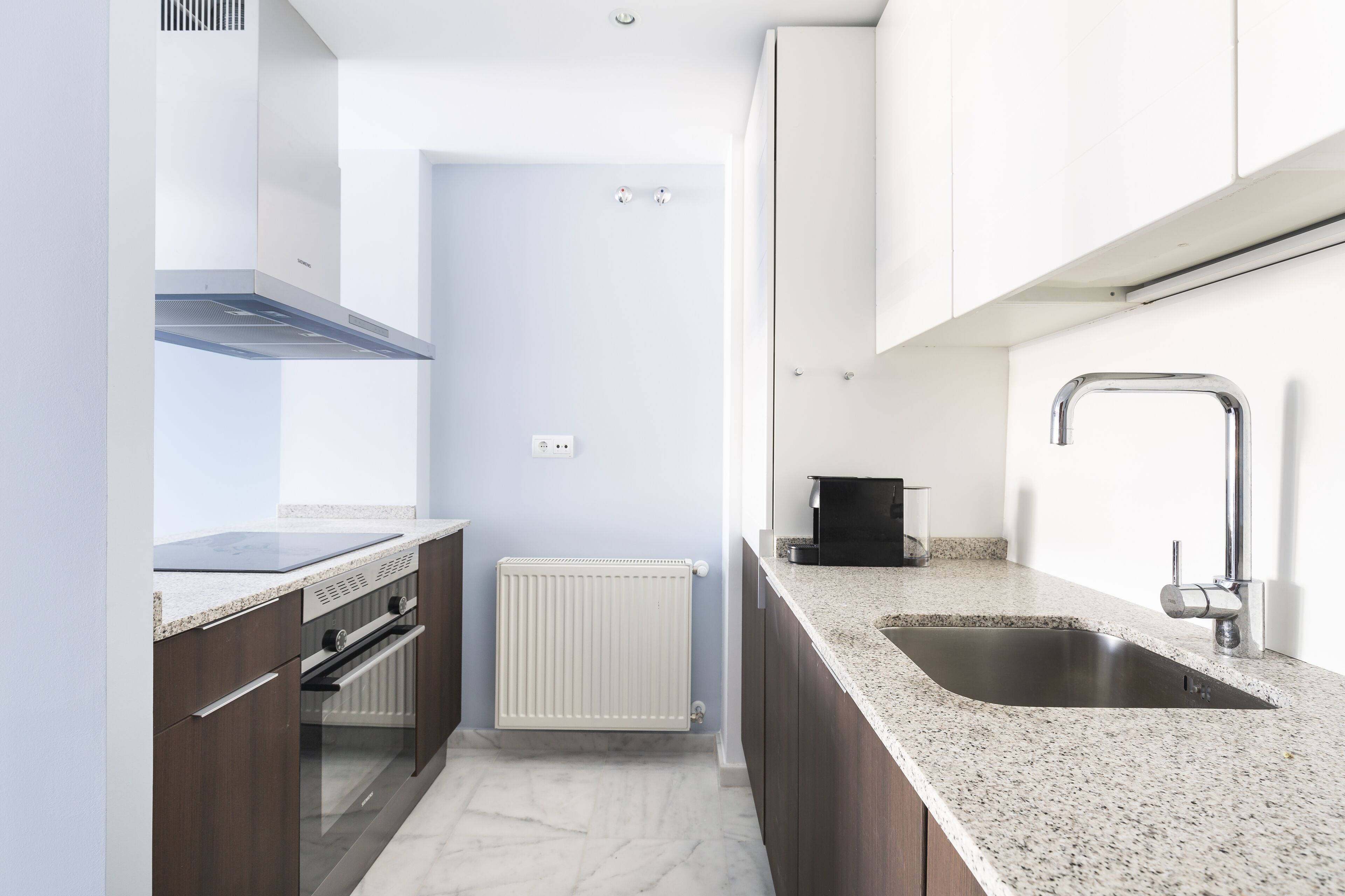Une cuisine moderne dotée d’un four encastré, d’un évier en acier inoxydable et d’un radiateur blanc.