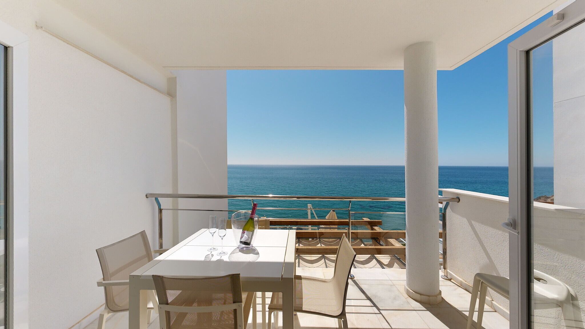 A balcony with a table set for two, overlooking the sea.
