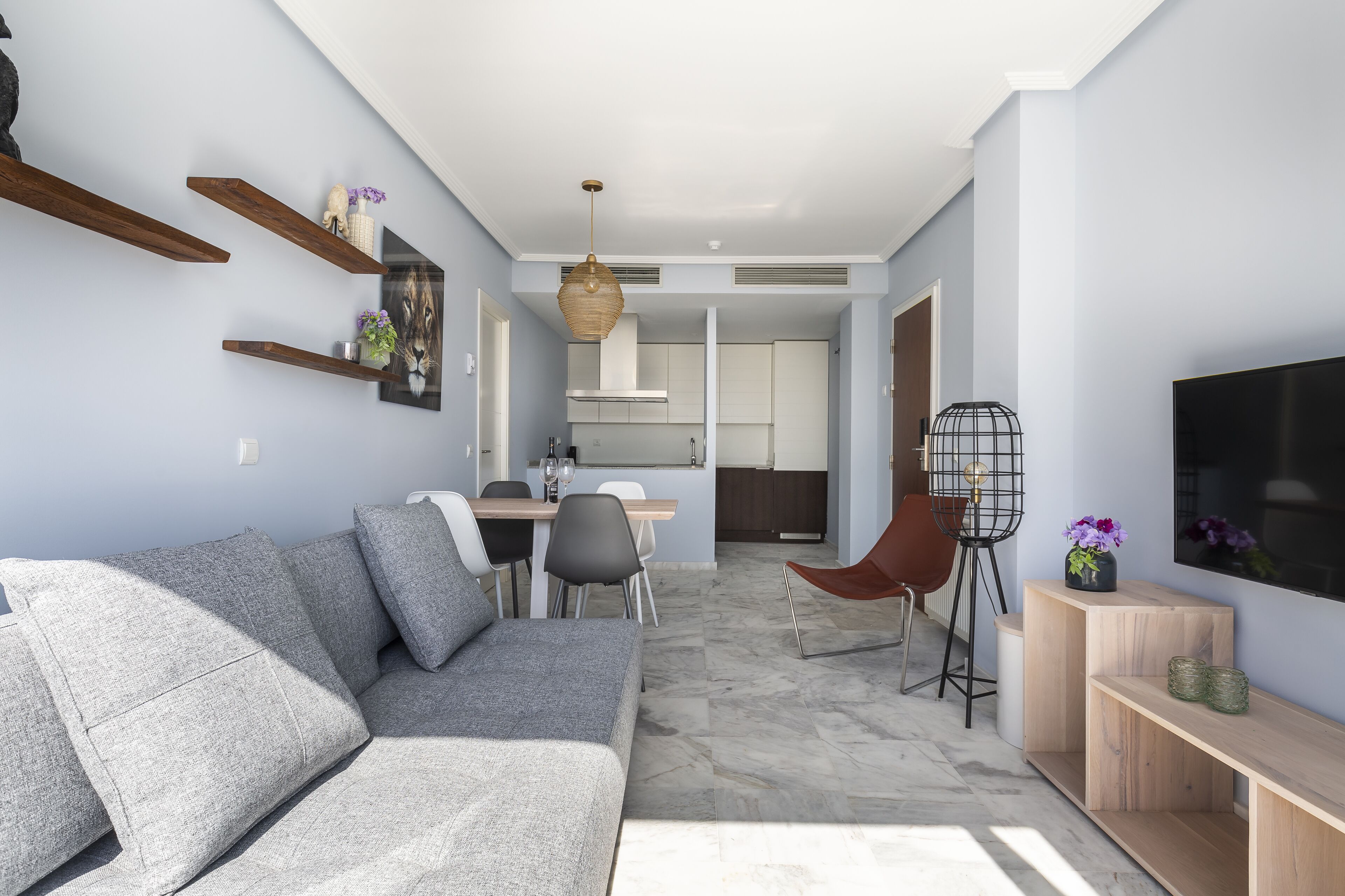 Ein modernes Wohnzimmer mit grauem Sofa, Holzböden, einem Essbereich mit Tisch und Stühlen sowie einer Küche im Hintergrund.