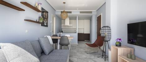 Ein modernes Wohnzimmer mit grauem Sofa, Holzböden, einem Essbereich mit Tisch und Stühlen sowie einer Küche im Hintergrund.