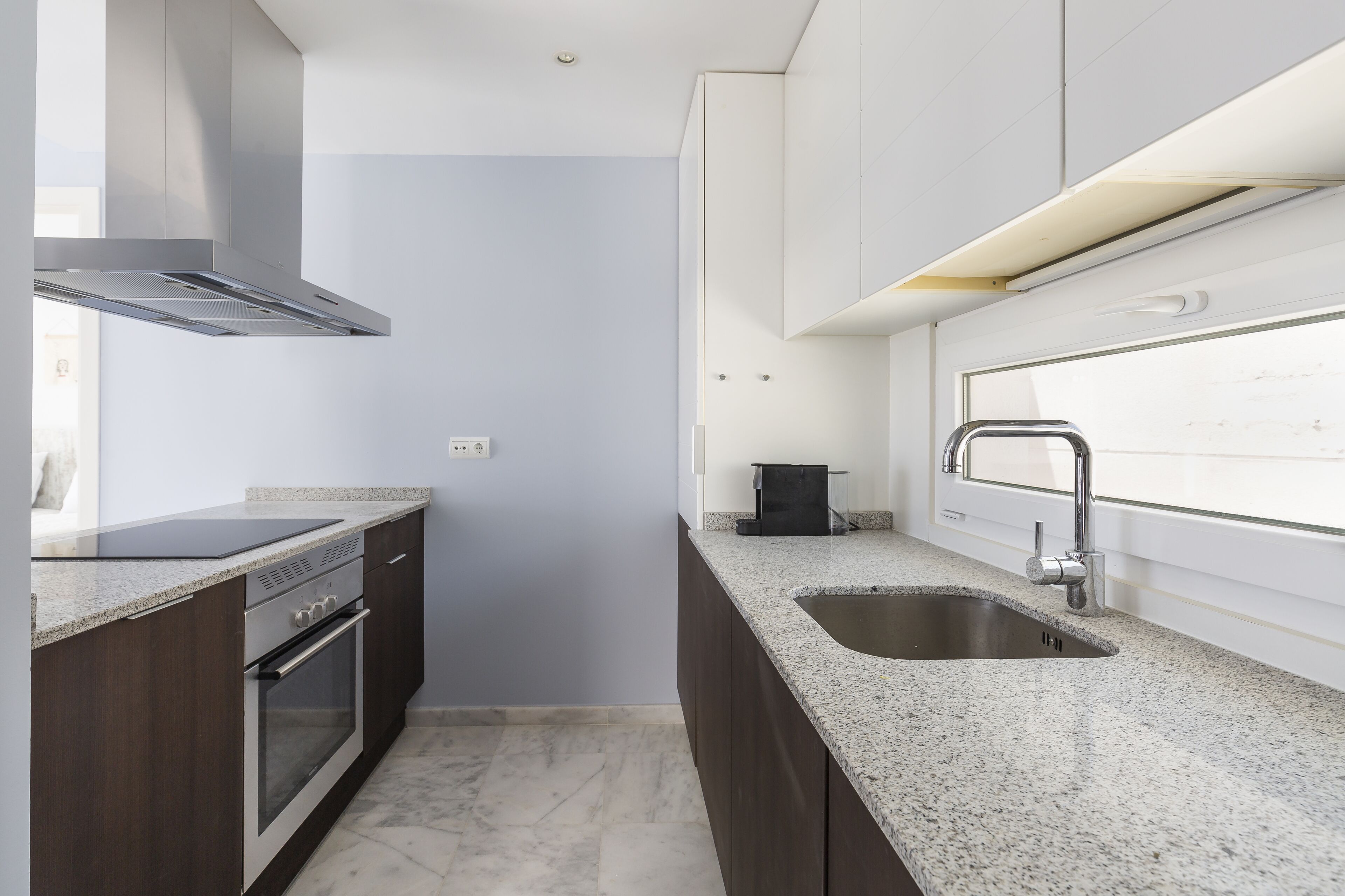 Una cocina moderna con armarios de madera oscura, una campana extractora de acero inoxidable, horno empotrado, encimera de granito, pileta doble y una ventana sobre la pileta.
