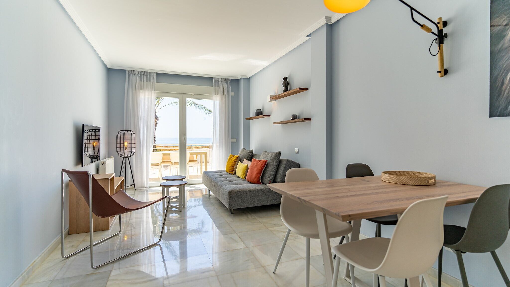 Una sala de estar moderna con un sofá, una mesa de comedor y sillas. Hay un balcón con vista al océano.
