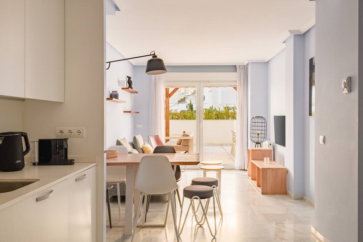 Een moderne keuken met een spoelbak, waterkoker en koffiezetapparaat, die uitkomt op een eethoek met een tafel, stoelen en uitzicht op het omliggende landschap.