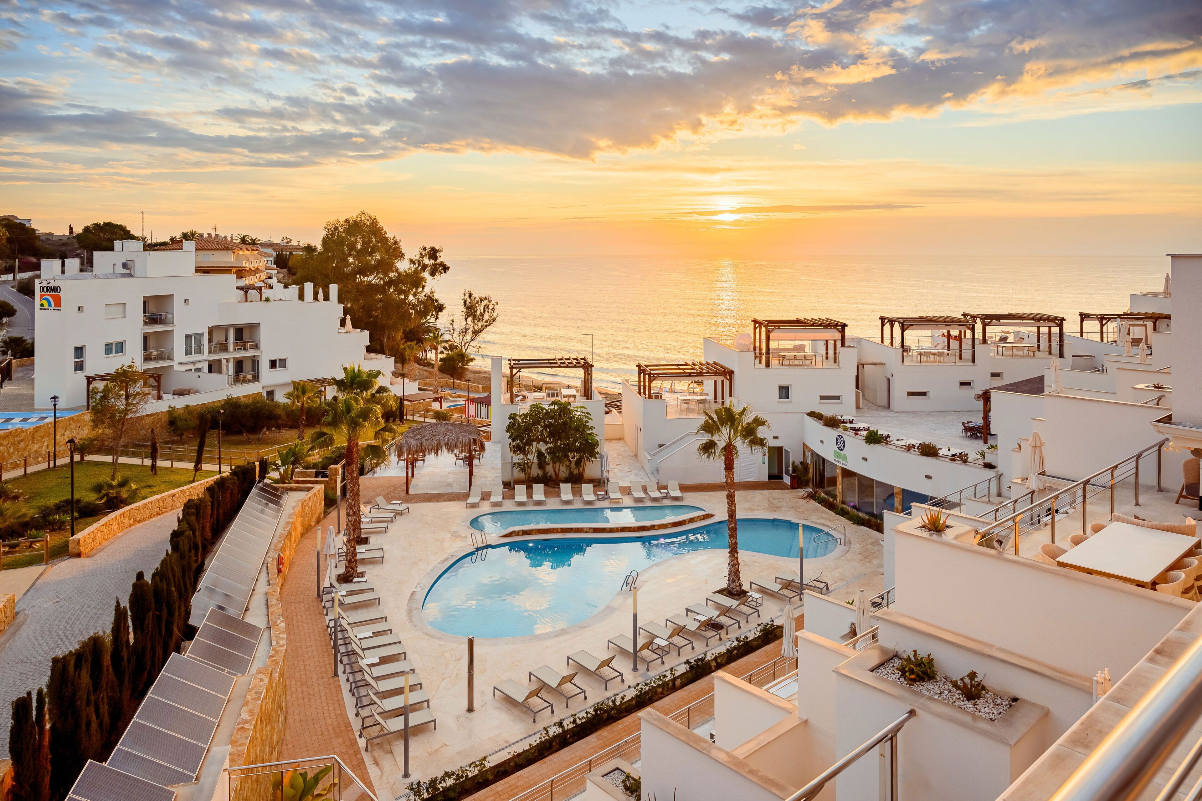A resort with a pool, lounge chairs, and a view of the sea at sunset.
