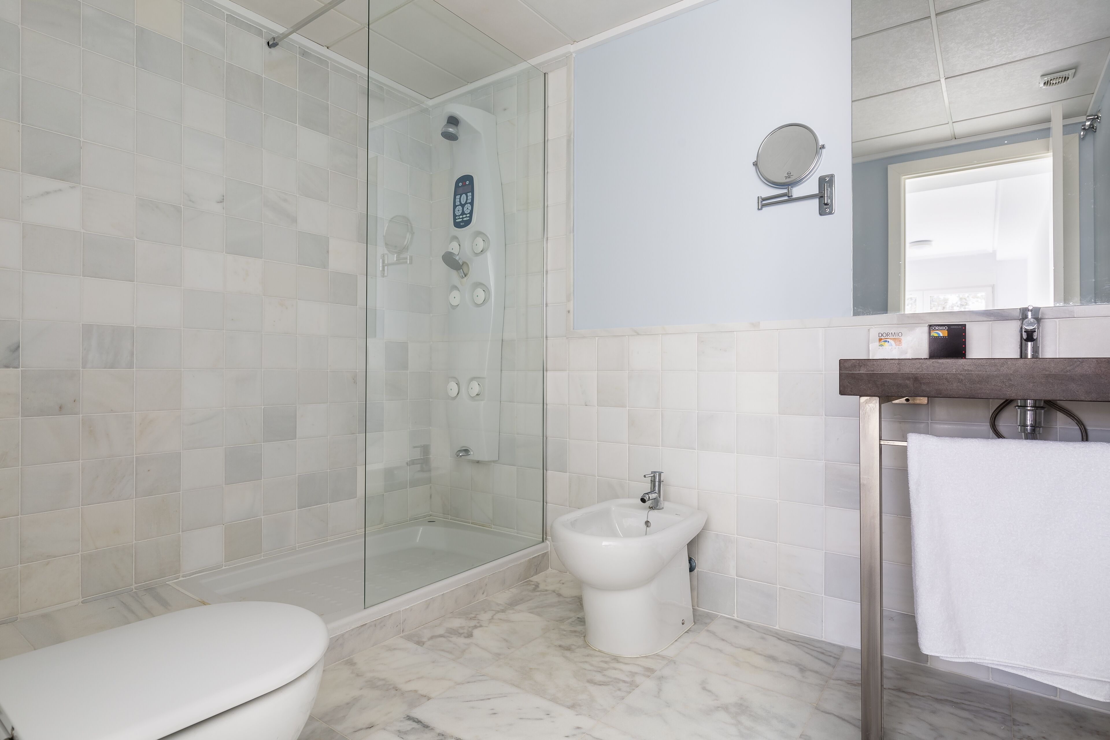A bathroom with a glass-enclosed shower, a bidet, a toilet, and a sink with a mirror.