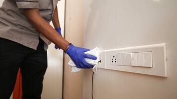 A person cleaning a wall-mounted electrical outlet with a cloth.