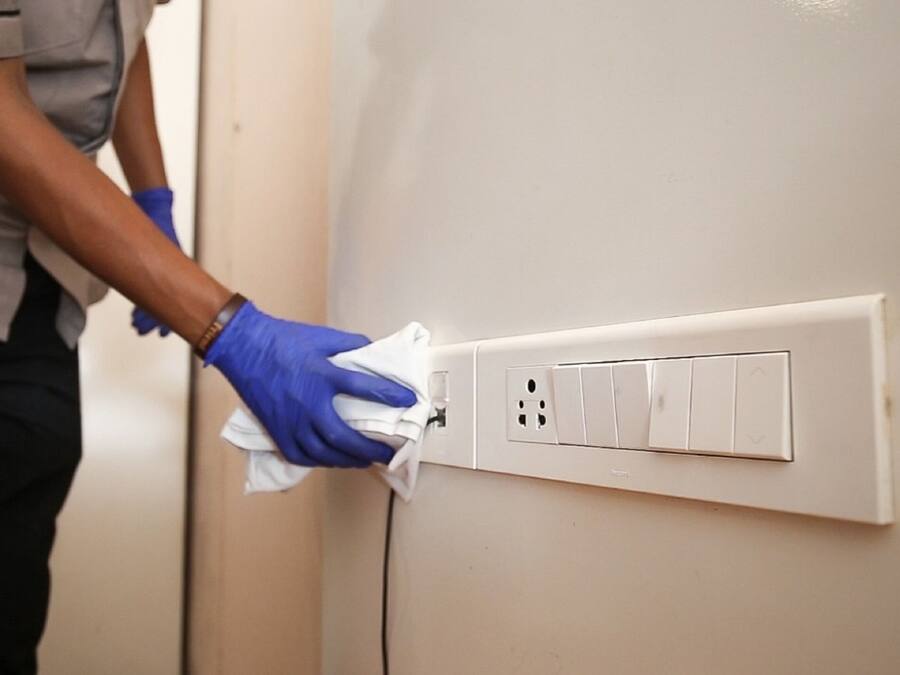 A person cleaning a wall-mounted electrical outlet with a cloth.