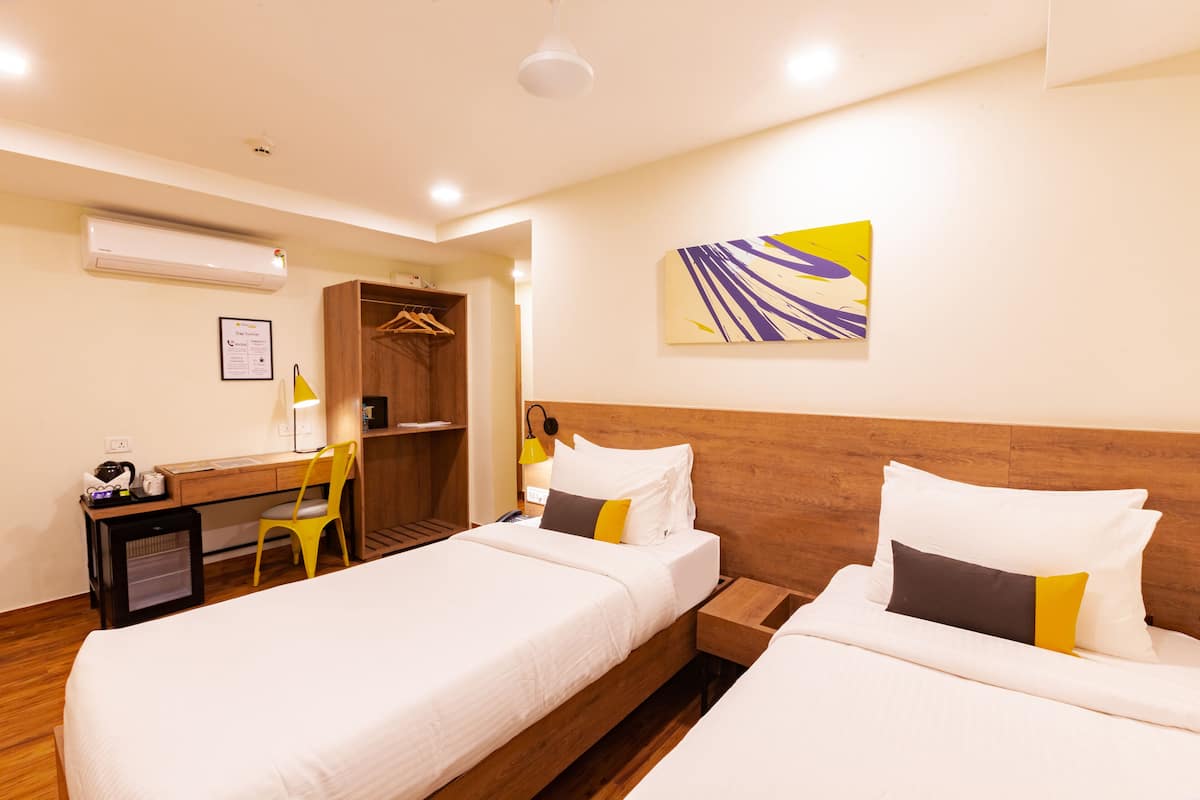 A hotel room with two beds, a desk, a chair, a wardrobe, and a painting on the wall.