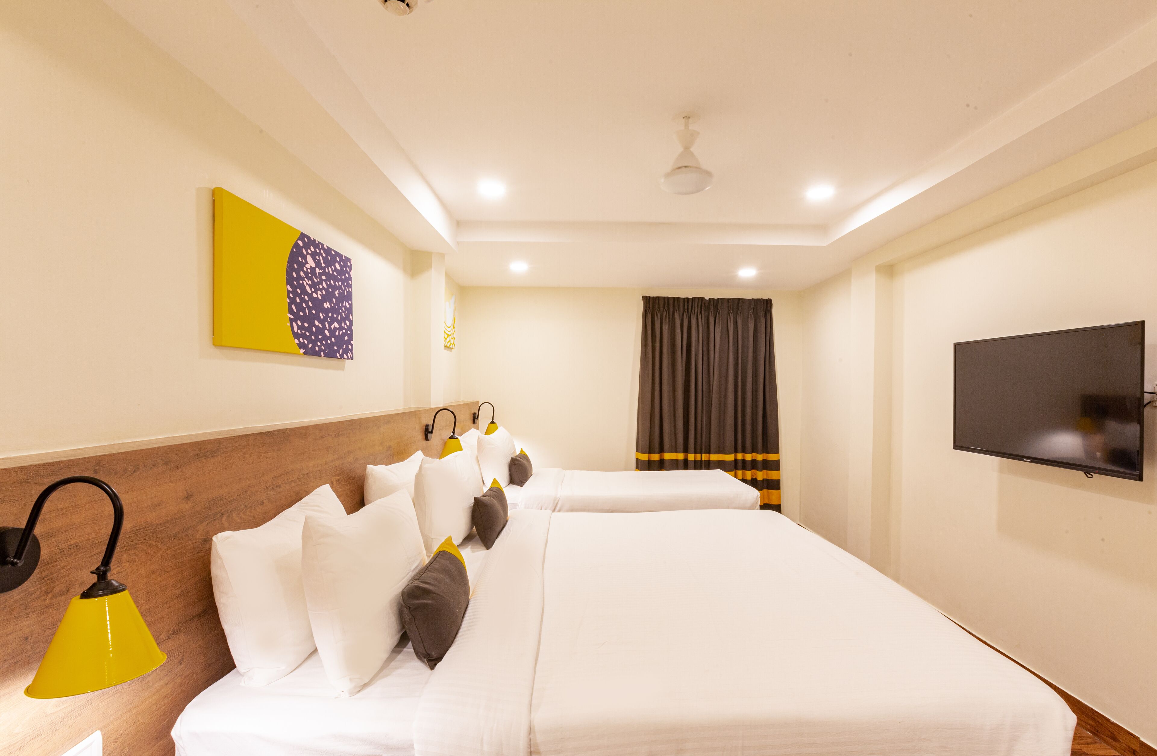 A hotel room with two beds, a flat-screen TV, a ceiling fan, and a painting on the wall.