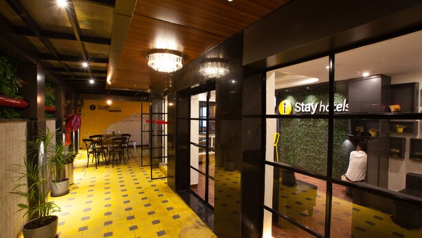 A hotel lobby with a yellow patterned floor, potted plants, and a reception desk. - IStayHotels  Jubilee Hills  Hyderabad (Hyderabad)