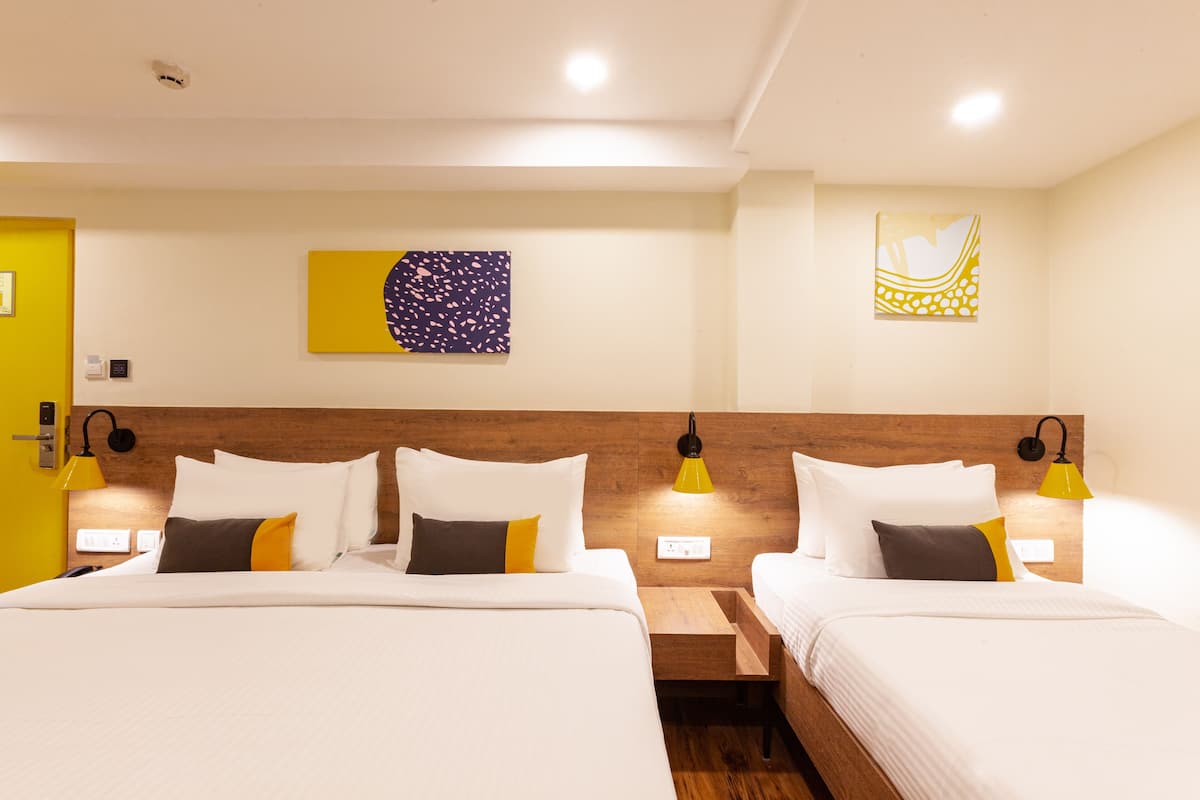A hotel room with two beds, each with white bedding and a wooden headboard. There are wall-mounted lamps on either side of the beds, and artwork is displayed on the walls.