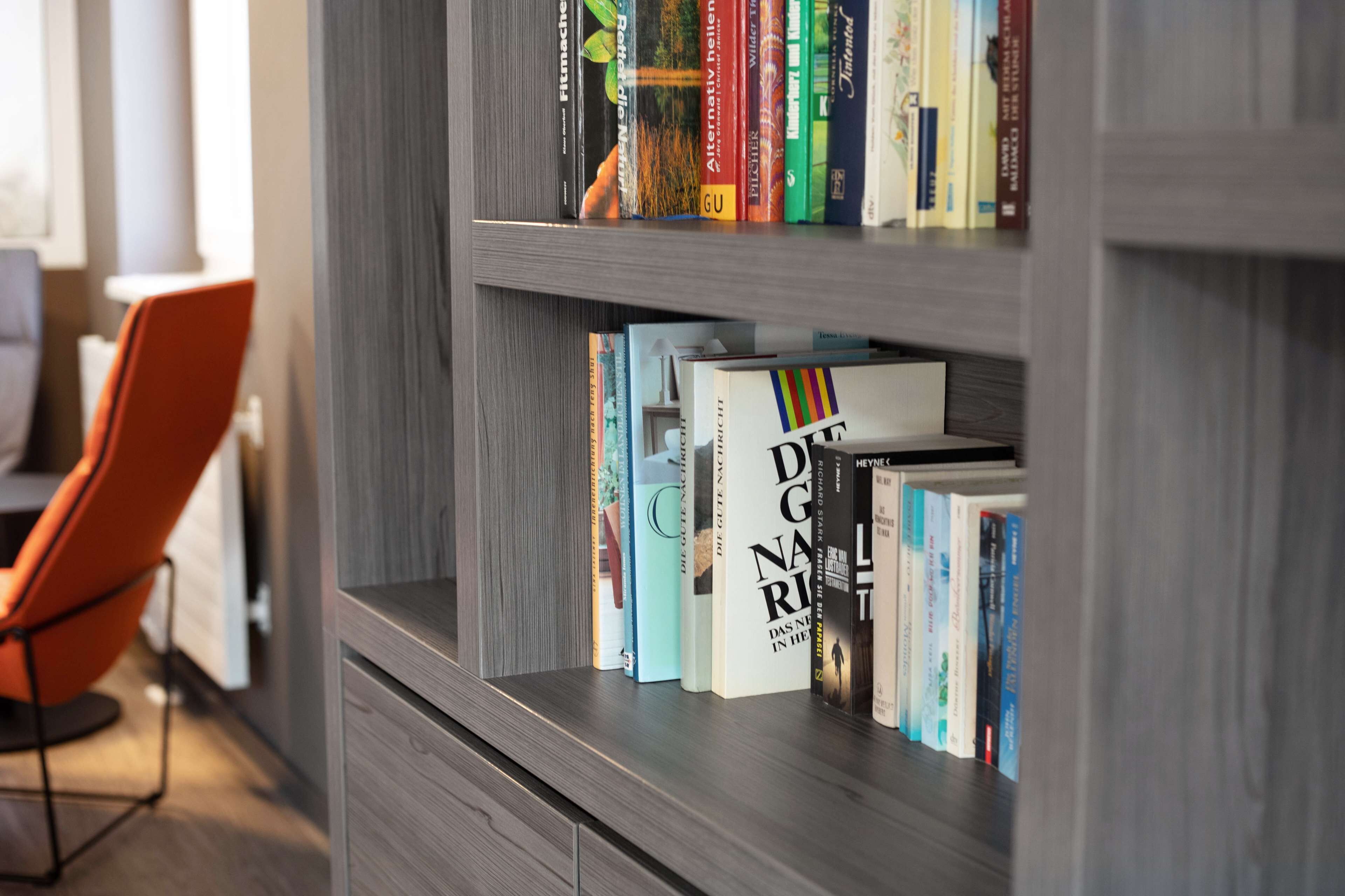 A bookshelf with various books, a modern chair, and a wooden cabinet.