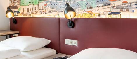 Habitación de hotel con dos camas, un mural de paisaje urbano en la pared y dos lámparas de pared.