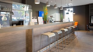 A modern reception area with a wooden counter, bar stools, and pendant lighting. - Campanile Duisburg City (Duisburg)