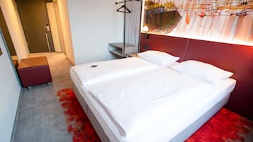 Ein Hotelzimmer mit einem Bett, einer Bank, einem Kleiderständer und einer Wandlampe.