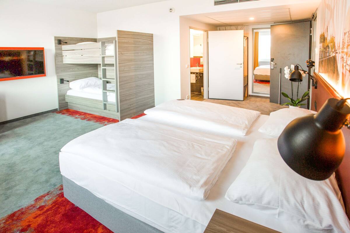 Habitación de hotel con una cama grande, un armario empotrado, baño con espejo y alfombra roja.
