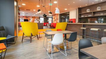 A modern dining area with a mix of seating options including chairs and tables, a bar area with shelves, and a visible kitchen in the background.