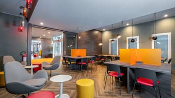 Un espace de restauration moderne avec des tables rondes, des chaises grises et rouges, et des tabourets jaunes.