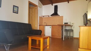 A living room with a black sofa, a wooden coffee table, a kitchen area with a stove, and a TV.
