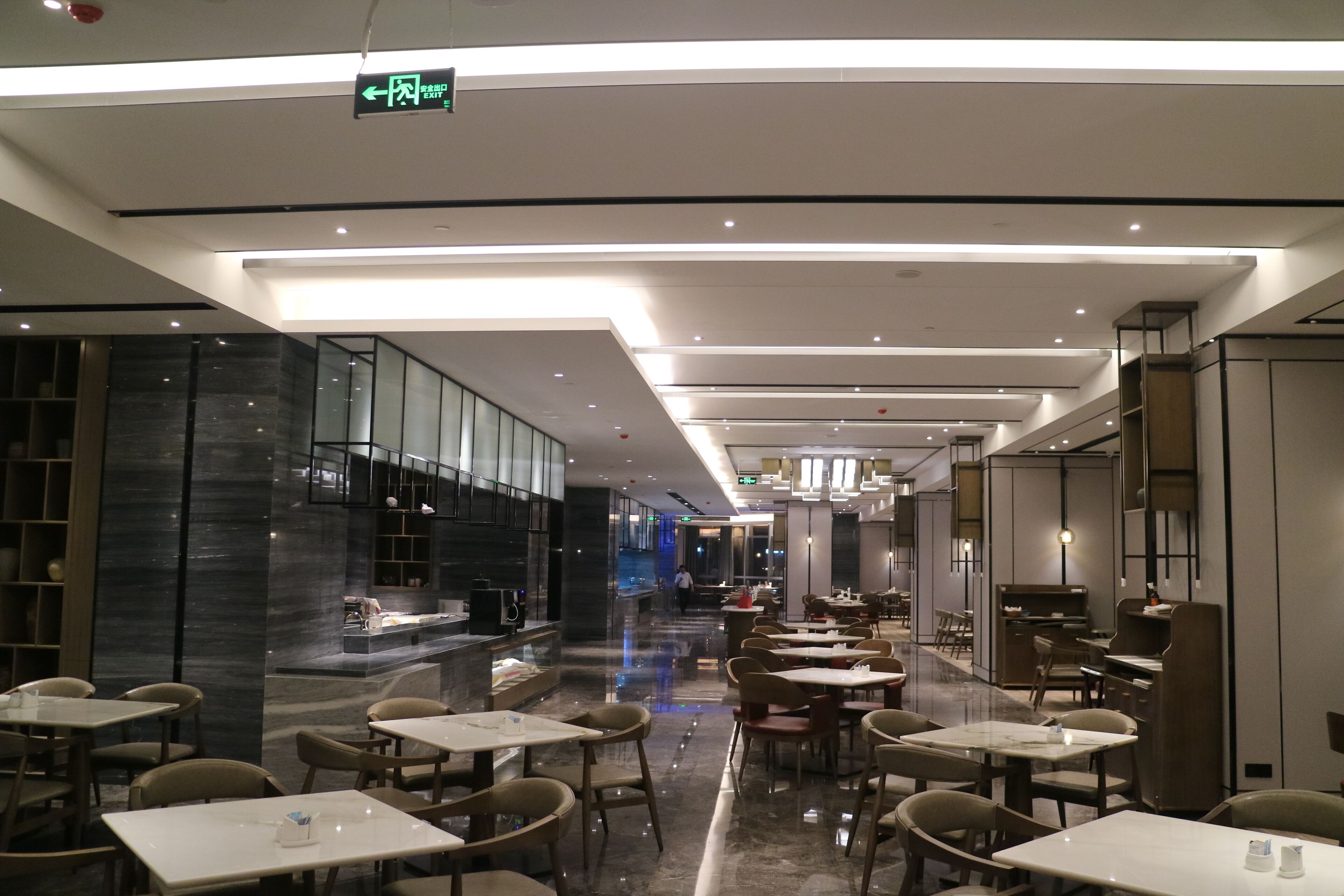 A modern restaurant with a clean, minimalist design, featuring a long counter and multiple dining tables.