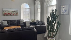 A living room with two black leather sofas, a wooden coffee table, a large cactus plant, and a chandelier. - OYO Gran Canaria Hotel (Folkestone)