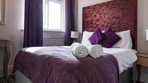 A neatly made bed with a purple blanket, two rolled towels, and two purple pillows. - OYO Gran Canaria Hotel (Folkestone)