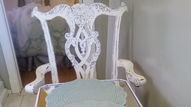A white ornate chair with a glass table in front.
