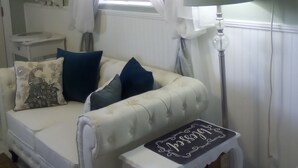 A cozy living room with a white sofa, a small side table, a floor lamp, and a window with sheer curtains.