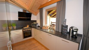 A modern kitchen with white cabinets, a wooden ceiling, a built-in oven, a microwave, and a coffee machine.
