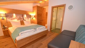 A wooden bedroom with a bed, a nightstand, a sofa, and a shower area.