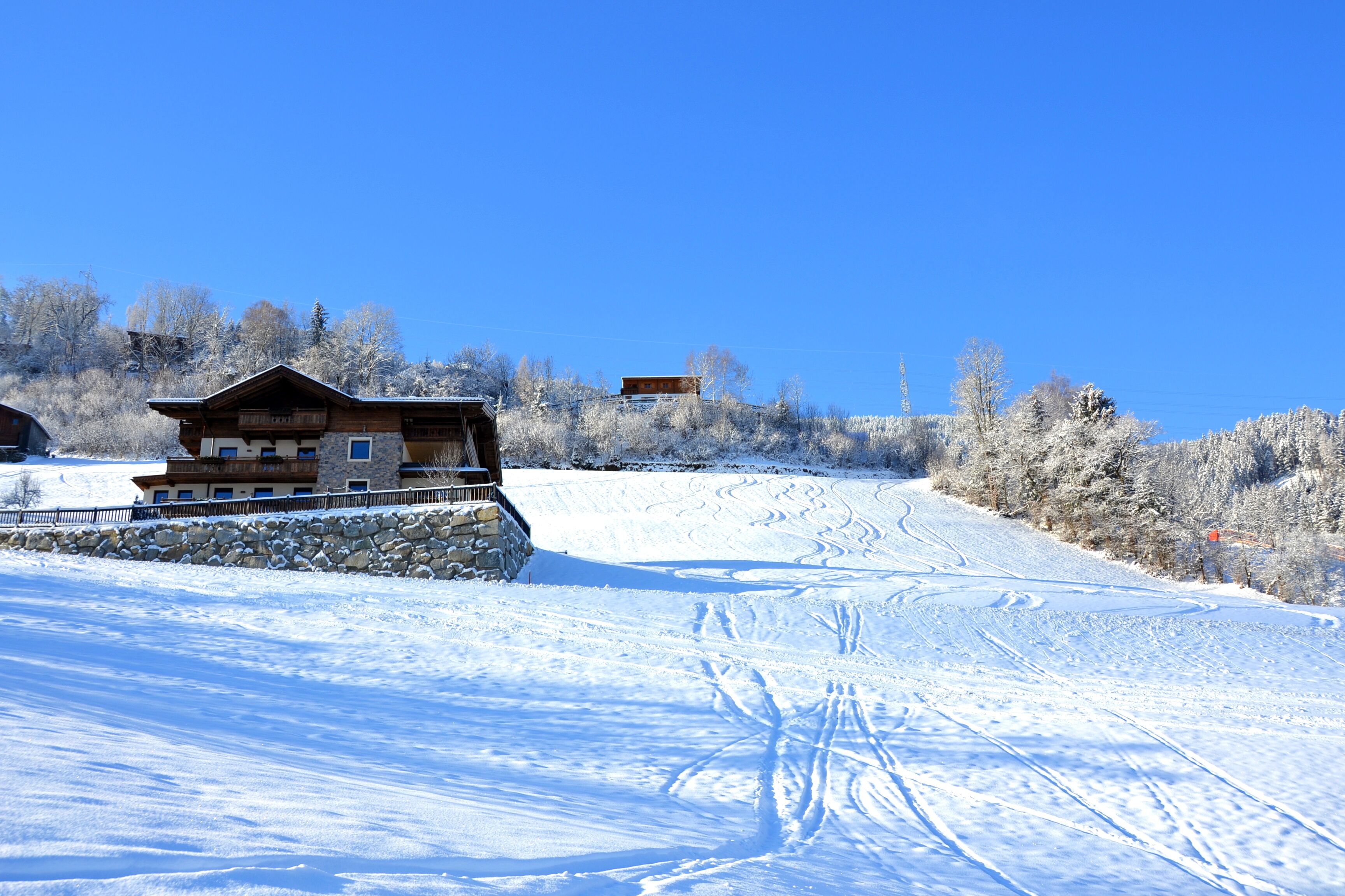A wooden chalet with a stone foundation, situated on a snow-covered slope with ski tracks.