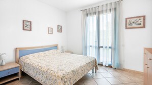 Une chambre à coucher avec un lit, une table de chevet, une commode et une fenêtre avec des rideaux.