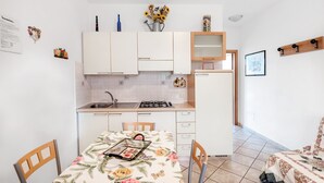 Une cuisine de taille réduite avec des meubles blancs, une table à manger recouverte d’une nappe à motifs floraux et un petit réfrigérateur.