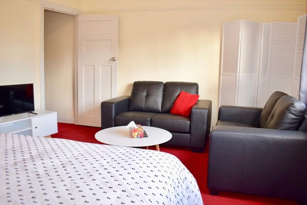 A hotel room with a bed, two sofas, a TV, and a small white table.