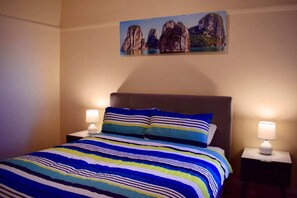 Habitación de hotel con cama, ropa de cama a rayas, dos lámparas de noche y un cuadro de formaciones rocosas en la pared.