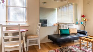 A living room with a black leather sofa, a wooden table, a white chair, and a small wooden table with a red cushion. - Charming 1 Bedroom Apartment in Vibrant South Yarra (South Yarra)