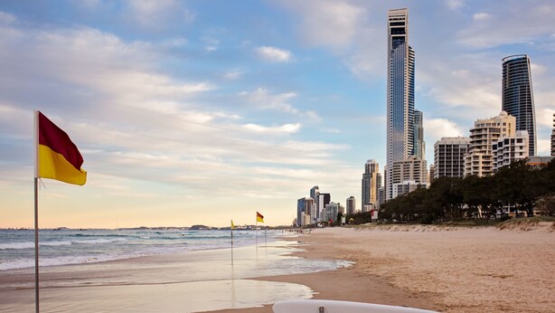 A beach with a lifeguard stand and a surfboard, a flag, and a city skyline in the background. - Charming 1 Bedroom Apartment in Vibrant South Yarra (South Yarra)