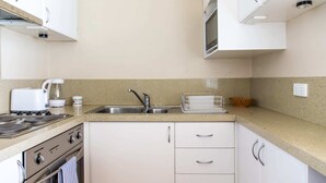 A kitchen with white cabinets, a stainless steel sink, a stove, and a coffee maker. - Charming 1 Bedroom Apartment in Vibrant South Yarra (South Yarra)