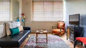 A modern living room with a black sofa, a wooden coffee table, a red chair, a television, and a cabinet. - Charming 1 Bedroom Apartment in Vibrant South Yarra (South Yarra)