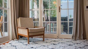 A room with a beige armchair, a white and blue patterned rug, and a view through a glass door to the outside. - Cosy 3 Bedroom Villa in Freeman's Bay (Auckland)