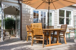 A wooden deck with a table and chairs under a large umbrella, surrounded by white walls and windows. - Cosy 3 Bedroom Villa in Freeman's Bay (Auckland)