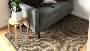 Ein graues Sofa mit einer kleinen Pflanze auf einem Holzschemel, einem gemusterten Kissen und einem Strandbild an der Wand.